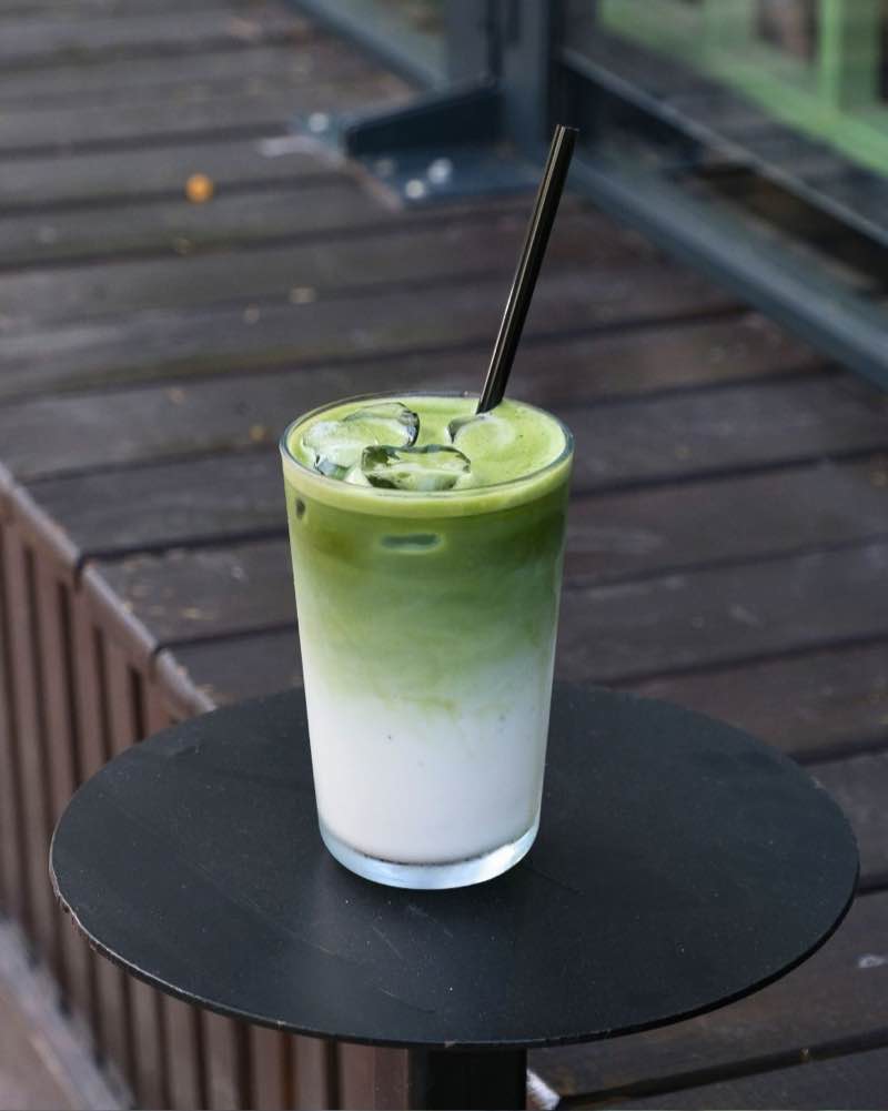 An iced matcha latte with a black straw on a small round table outdoors